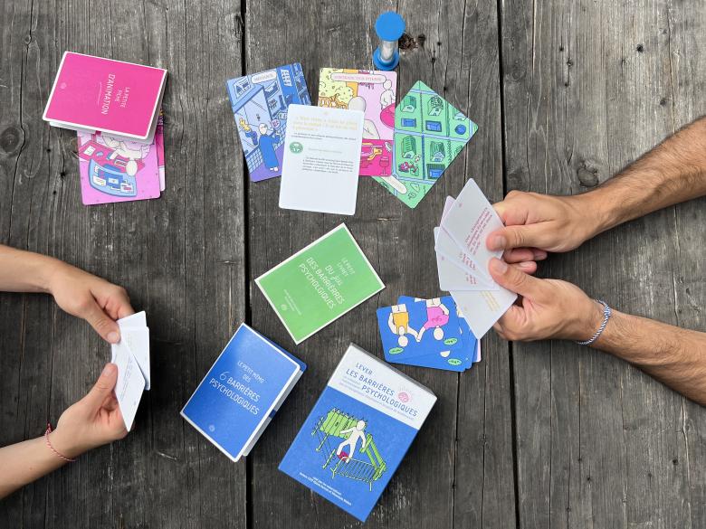 Illustration de la formation "Comment communiquer sur le changement climatique et la perte de biodiversité". Deux personnes jouent à un jeu de carte pédagogique sur les barrières psychologiques.